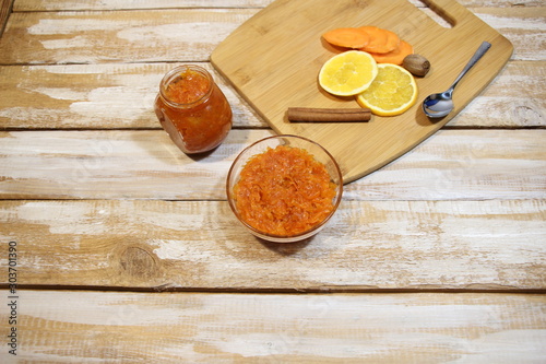Carrot and orange jam on glass bowl and pot with spoon, ingredients on wooden background