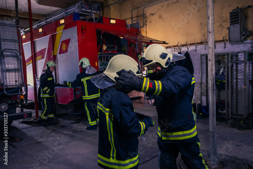 Firefighters preparing their uniform and the firetruck in the background inside the fire station
