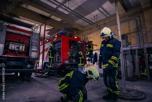 Firefighters preparing their uniform and the firetruck in the background inside the fire station