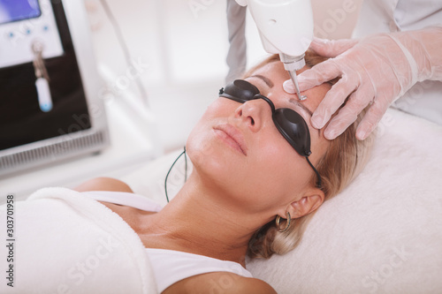 Close up of a mature woman getting her eyebrow tattoo removed at cosmetology clinic. Dermatologist removing tattooed eyebrows on a female client using laser