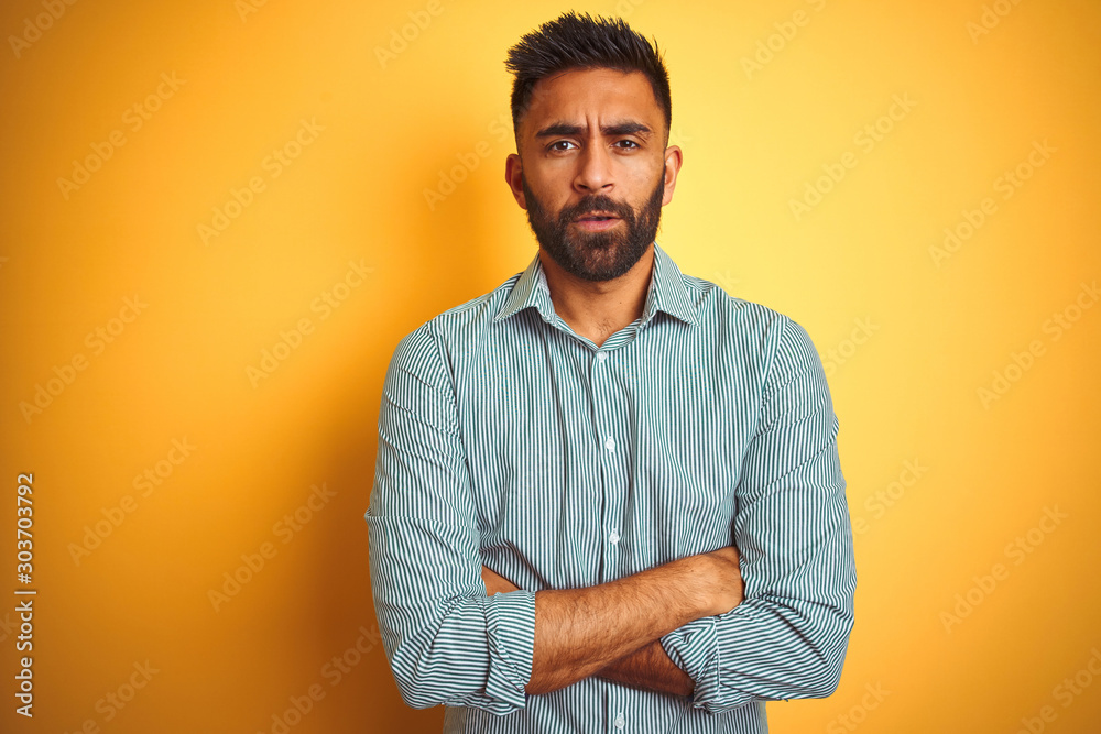 Young indian man wearing green striped shirt standing over isolated yellow background skeptic and nervous, disapproving expression on face with crossed arms. Negative person. Young indian man wearing green striped shirt standing over isolated yellow background skeptic and nervous, disapproving expression on face with crossed arms. Negative person.