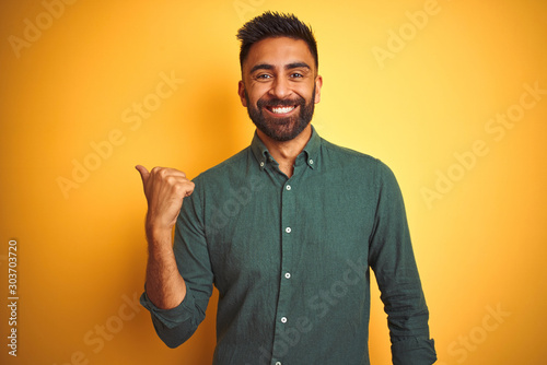 Young indian businessman wearing elegant shirt standing over isolated white background smiling with happy face looking and pointing to the side with thumb up.