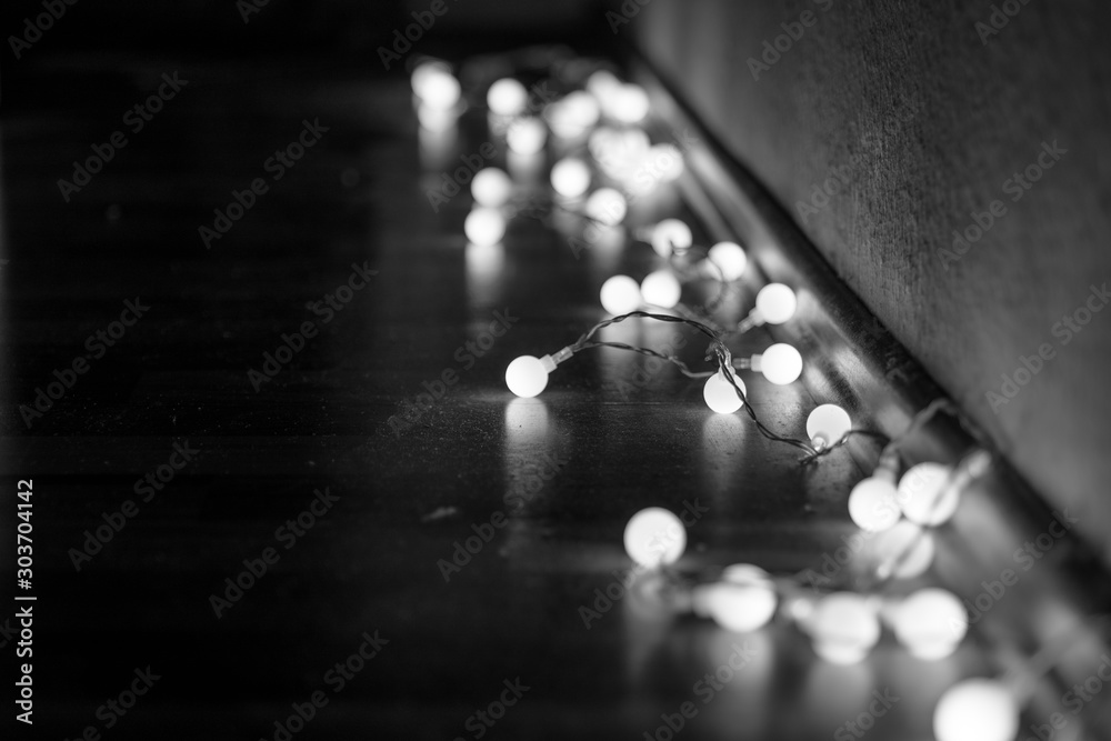 Εκτύπωση καμβά Black and white mood and tone of close up view of decorative wire led small warm white light bulbs lay on a floor at corner of dark and dim room