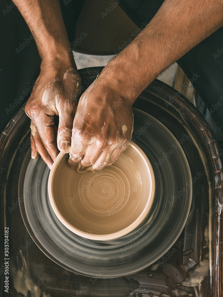 Fototapeta Pottery workshop Top view Man is sculpting a bowl behind a rotating potter's whe