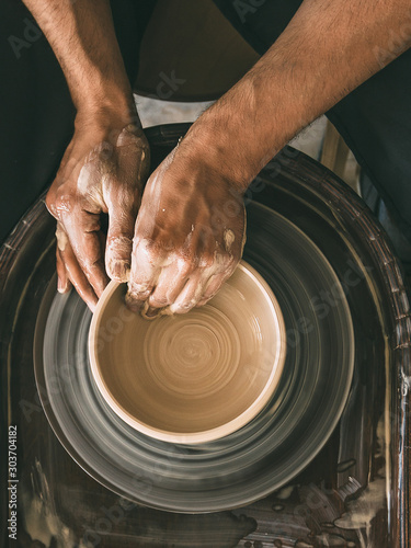 Fotografia Pottery workshop Top view Man is sculpting a bowl behind a rotating potter's whe