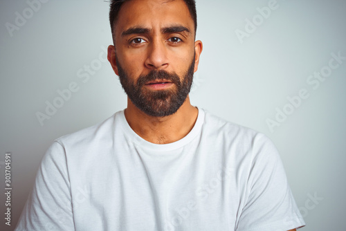 Young indian man wearing t-shirt standing over isolated white background skeptic and nervous, disapproving expression on face with crossed arms. Negative person.