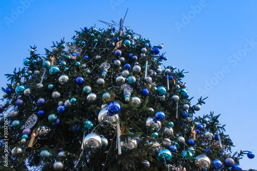A large Christmas tree decorated with a star and round balls on a blue sky background. Happy New Year.