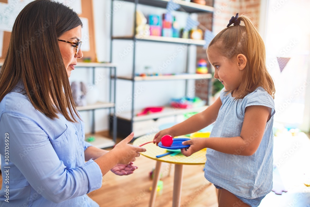 Caucasian girl kid playing and learning at playschool with female teacher. Mother and daughter playing cooking