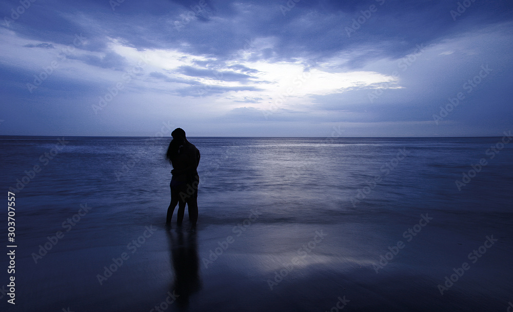 couple standing in the sea at sunset blue tones