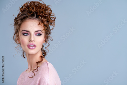 Young girl with wavy hair looks away. Portrait of a beautiful woman with a brown hair. Young  model with beautiful brown hair, posing at studio. Young woman with bright eye make-up looks away