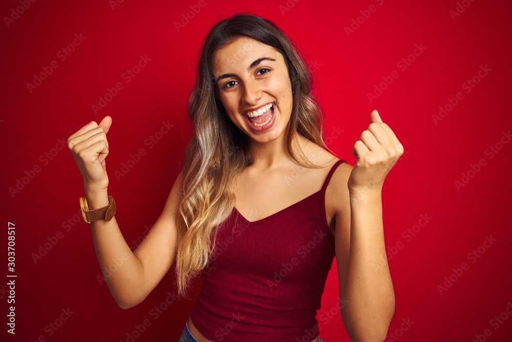 Young beautiful woman wearing a t-shirt over red isolated background celebrating surprised and amazed for success with arms raised and open eyes. Winner concept. Young beautiful woman wearing a t-shirt over red isolated background celebrating surprised and amazed for success with arms raised and open eyes. Winner concept.