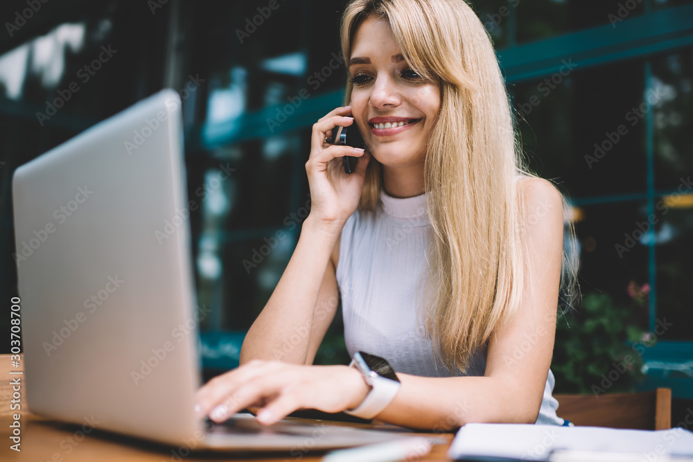Smiling freelancer speaking on phone and using laptop Smiling freelancer speaking on phone and using laptop