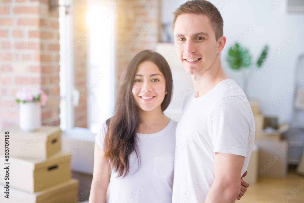 Young beautiful couple standing at new home around cardboard boxes Young beautiful couple standing at new home around cardboard boxes