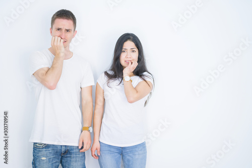 Young beautiful couple wearing casual t-shirt standing over isolated white background looking stressed and nervous with hands on mouth biting nails. Anxiety problem.
