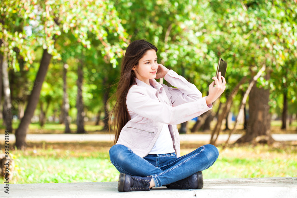 Brunette girl photographs herself on a cell phone while sitting in an autumn park. Brunette girl photographs herself on a cell phone while sitting in an autumn park.