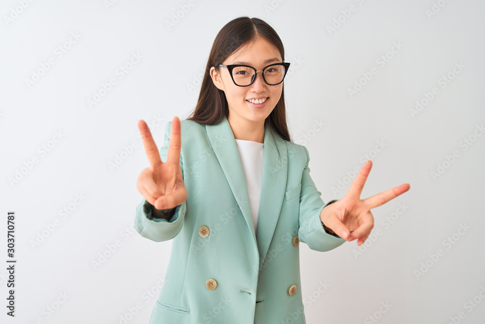 Chinese businesswoman wearing elegant jacket and glasses over isolated white background smiling looking to the camera showing fingers doing victory sign. Number two. Chinese businesswoman wearing elegant jacket and glasses over isolated white background smiling looking to the camera showing fingers doing victory sign. Number two.