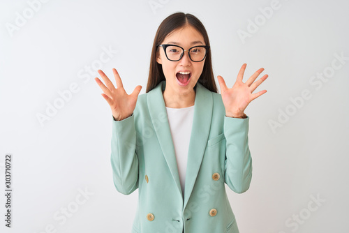 Chinese businesswoman wearing elegant jacket and glasses over isolated white background celebrating crazy and amazed for success with arms raised and open eyes screaming excited. Winner concept