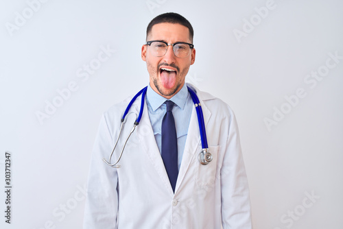 Young doctor man wearing stethoscope over isolated background sticking tongue out happy with funny expression. Emotion concept. © Krakenimages.com