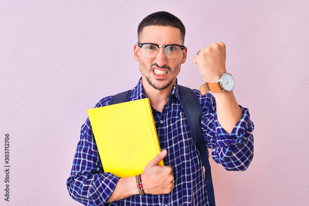 Young handsome student man holding a book over isolated background annoyed and frustrated shouting with anger, crazy and yelling with raised hand, anger concept Young handsome student man holding a book over isolated background annoyed and frustrated shouting with anger, crazy and yelling with raised hand, anger concept