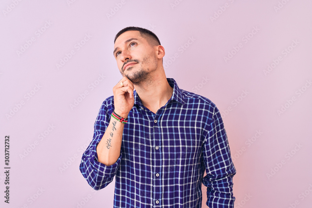 Young handsome man standing over isolated background with hand on chin thinking about question, pensive expression. Smiling with thoughtful face. Doubt concept. Young handsome man standing over isolated background with hand on chin thinking about question, pensive expression. Smiling with thoughtful face. Doubt concept.