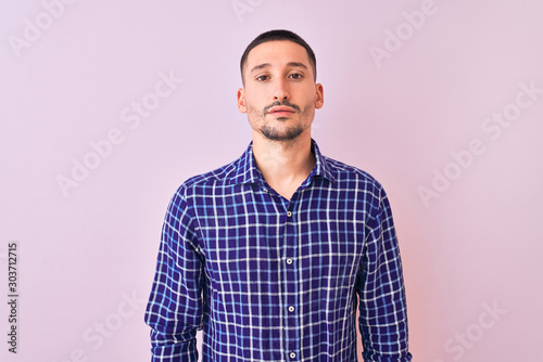 Young handsome man standing over isolated background Relaxed with serious expression on face. Simple and natural looking at the camera.