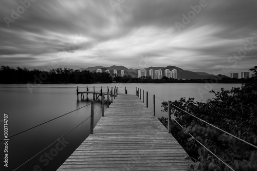 Long exposure of pier in calm lake, with nature all around, water is silky smooth, black and white
