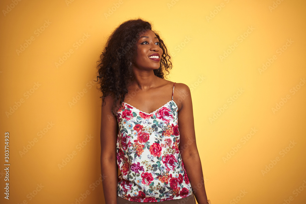 African american woman wearing floral summer t-shirt over isolated yellow background looking away to side with smile on face, natural expression. Laughing confident. African american woman wearing floral summer t-shirt over isolated yellow background looking away to side with smile on face, natural expression. Laughing confident.