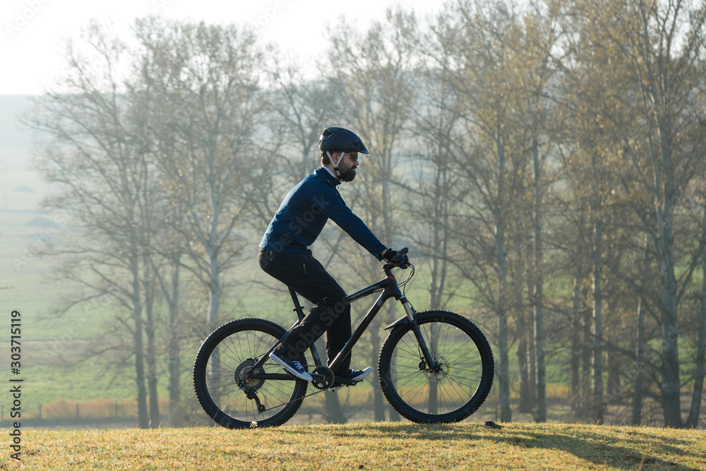 Cyclist in pants and fleece jacket on a modern carbon hardtail bike with an air suspension fork rides off-road.	