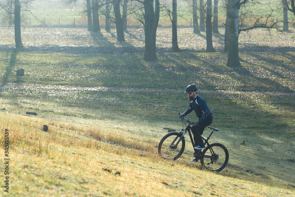 Cyclist in pants and fleece jacket on a modern carbon hardtail bike with an air suspension fork rides off-road.	