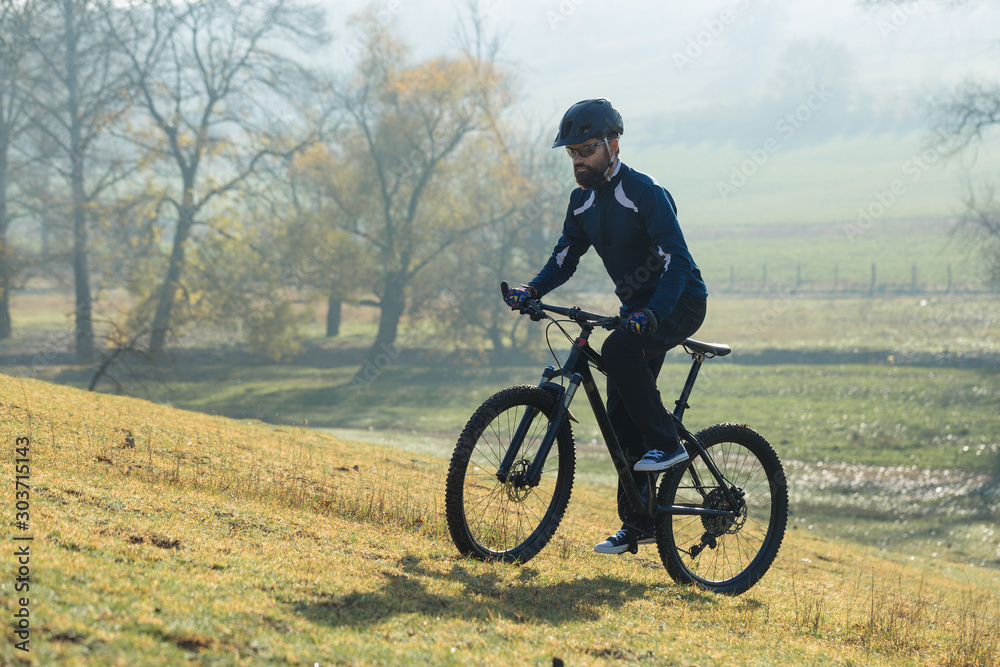 Cyclist in pants and fleece jacket on a modern carbon hardtail bike with an air suspension fork rides off-road.	