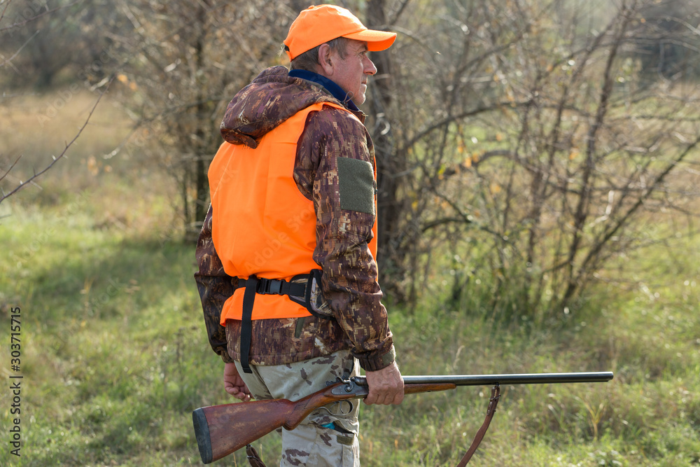 Hunting period, autumn season open. A hunter with a gun in his hands in hunting clothes in the autumn forest in search of a trophy. A man stands with weapons and hunting dogs tracking down the game. Hunting period, autumn season open. A hunter with a gun in his hands in hunting clothes in the autumn forest in search of a trophy. A man stands with weapons and hunting dogs tracking down the game.