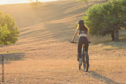 Girl on a mountain bike on offroad, beautiful portrait of a cyclist at sunset, Fitness girl rides a modern carbon fiber mountain bike in sportswear, a helmet, glasses and gloves. 