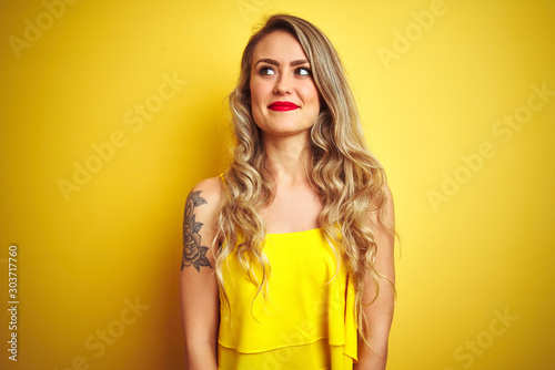 Young attactive woman wearing t-shirt standing over yellow isolated background smiling looking to the side and staring away thinking.