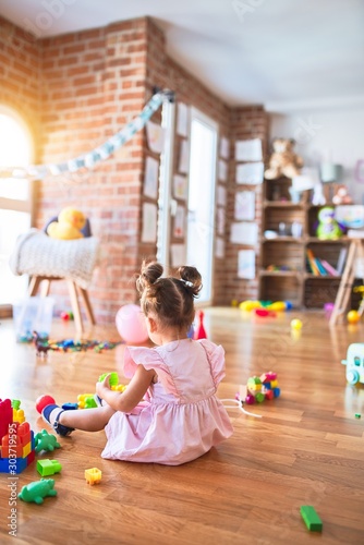 Young beautiful toddler sitting on the floor playing with building blocks at kindergaten photo