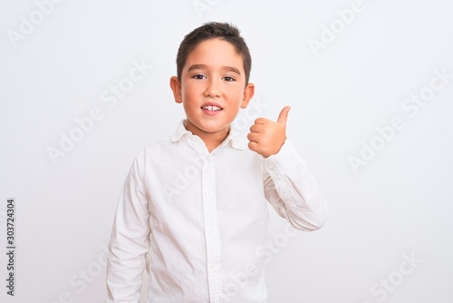 Beautiful kid boy wearing elegant shirt standing over isolated white background doing happy thumbs up gesture with hand. Approving expression looking at the camera with showing success.