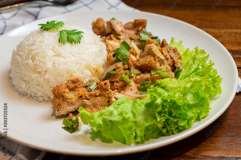 Rice with spicy chicken salad in white dish on wooden table.