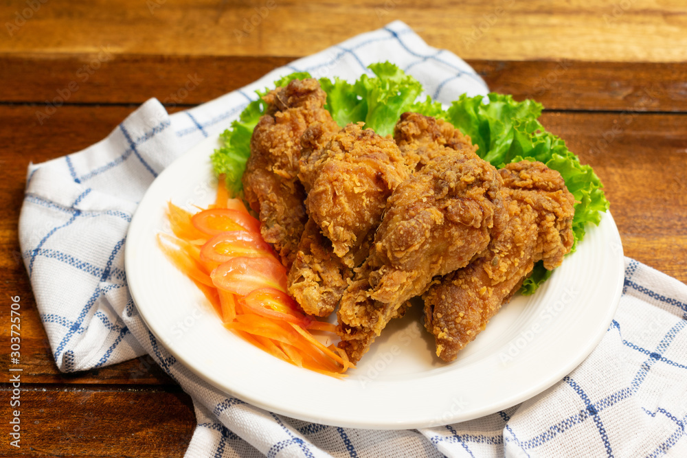 Fried chicken leg with tomato,carrot and lettuce in white dish on wooden table. Fried chicken leg with tomato,carrot and lettuce in white dish on wooden table.