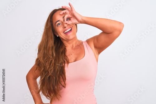 Middle age mature woman standing over white isolated background doing ok gesture with hand smiling, eye looking through fingers with happy face.