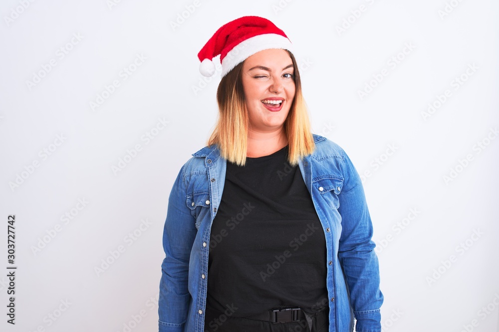 Young beautiful woman wearing Christmas Santa hat standing over isolated white background winking looking at the camera with sexy expression, cheerful and happy face. Young beautiful woman wearing Christmas Santa hat standing over isolated white background winking looking at the camera with sexy expression, cheerful and happy face.