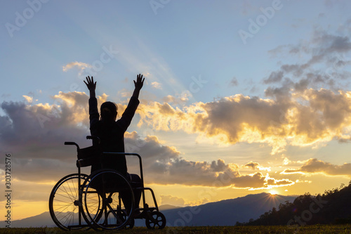 Happy disabled woman in a wheelchair and stretching hands at sunset. back view, © AungMyo