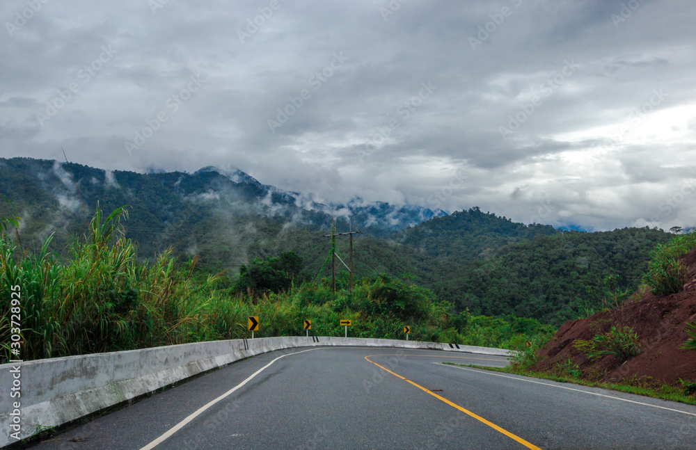 Blurred background of a mountain road view, from a car windscreen that runs with care, with natural scenery surrounded by plants, large trees