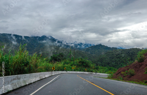 Blurred background of a mountain road view, from a car windscreen that runs with care, with natural scenery surrounded by plants, large trees