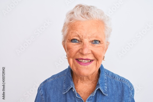 Senior grey-haired woman wearing casual denim shirt standing over isolated white background with a happy face standing and smiling with a confident smile showing teeth