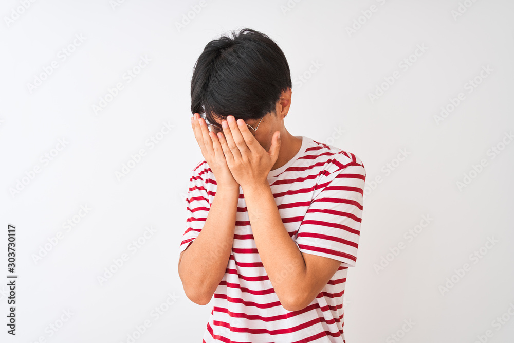 Young chinese man wearing glasses and striped t-shirt standing over isolated white background with sad expression covering face with hands while crying. Depression concept. Young chinese man wearing glasses and striped t-shirt standing over isolated white background with sad expression covering face with hands while crying. Depression concept.