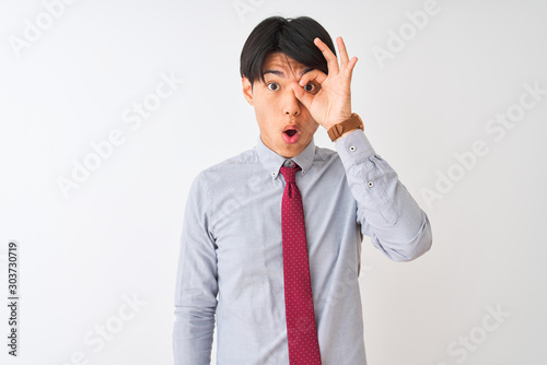 Chinese businessman wearing elegant tie standing over isolated white background doing ok gesture shocked with surprised face, eye looking through fingers. Unbelieving expression.