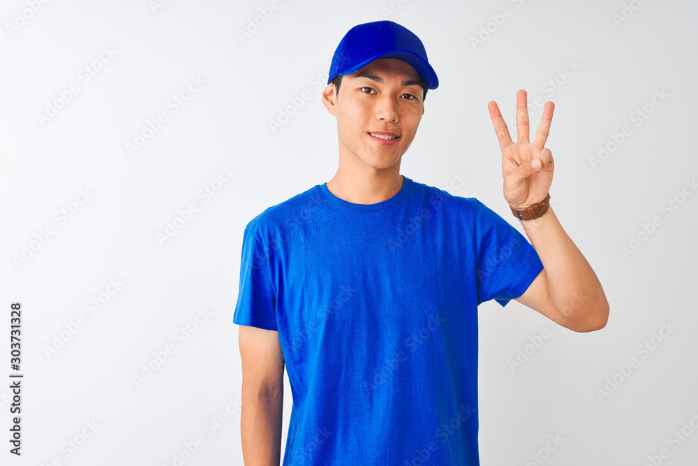 Chinese deliveryman wearing blue t-shirt and cap standing over isolated white background showing and pointing up with fingers number three while smiling confident and happy.