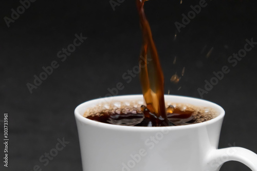 close-up pouring hot black coffee into a white cup, fresh coffee, black background