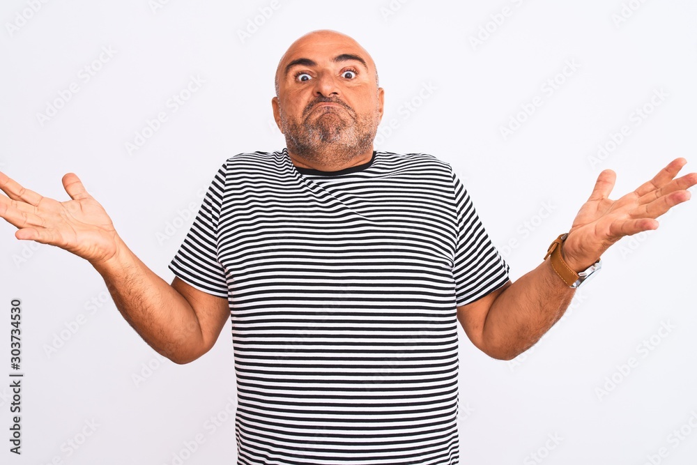 Middle age handsome man wearing striped navy t-shirt over isolated white background clueless and confused expression with arms and hands raised. Doubt concept.