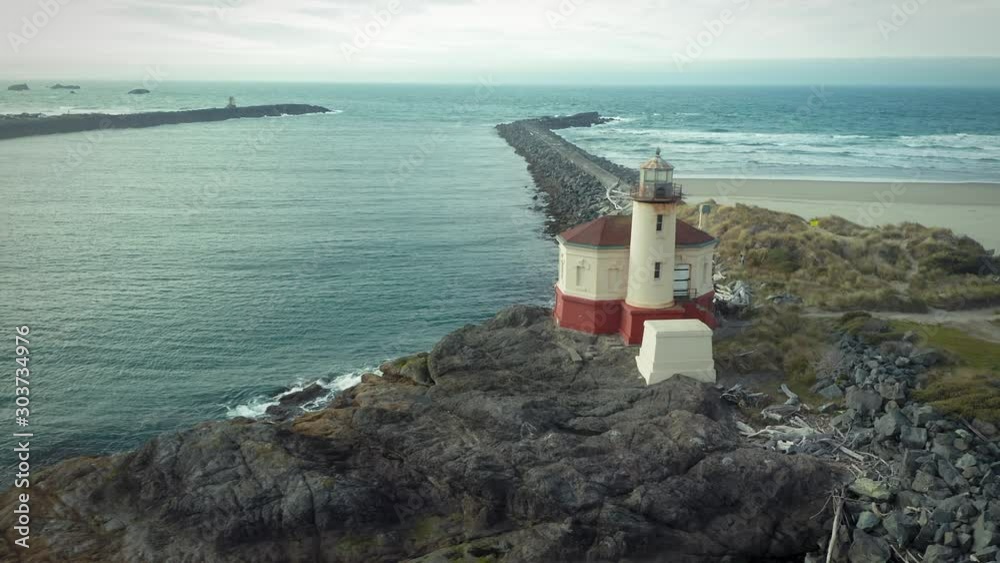 Aerial: Coquille River Lighthouse on a rocky shoreline in Bandon, Oregon, USA