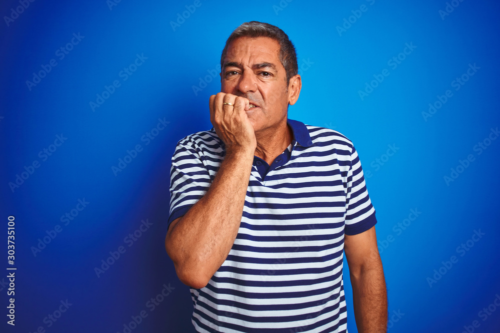 Handsome middle age man wearing striped polo standing over isolated blue background looking stressed and nervous with hands on mouth biting nails. Anxiety problem. Handsome middle age man wearing striped polo standing over isolated blue background looking stressed and nervous with hands on mouth biting nails. Anxiety problem.